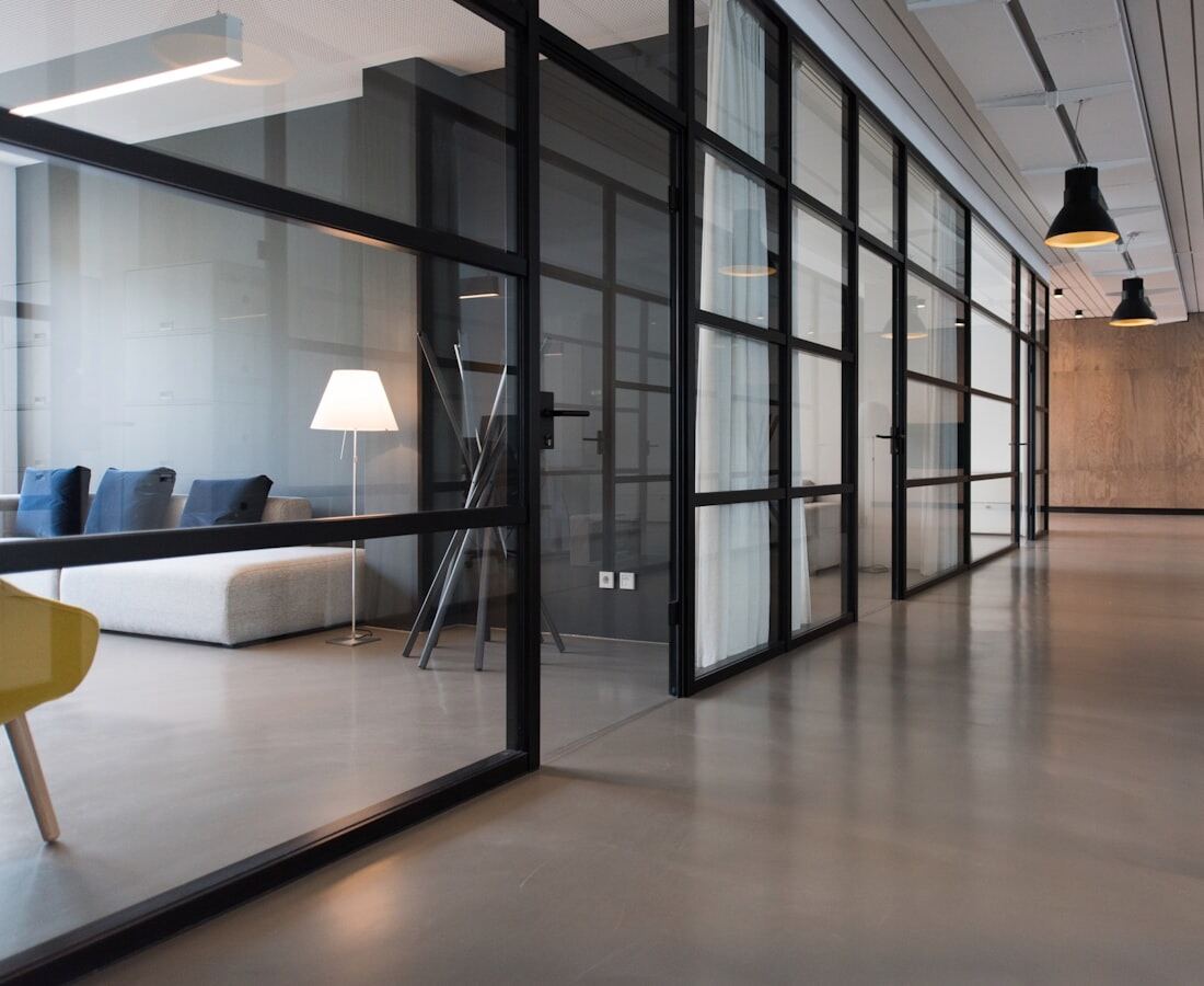 An office corridor in cool daylight, glass partitions along one side.